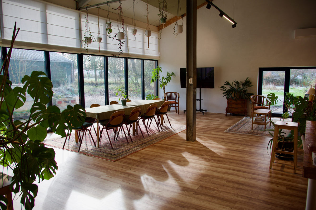 Lichte zaal in de voormalige koeienstal met een lange tafel, planten en grote ramen naar buiten
